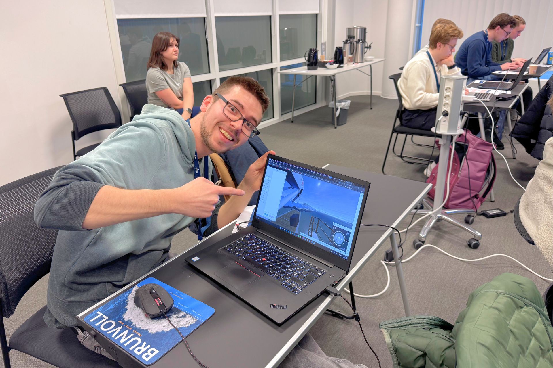 A smiling, male student displaying his work on a PC screen.