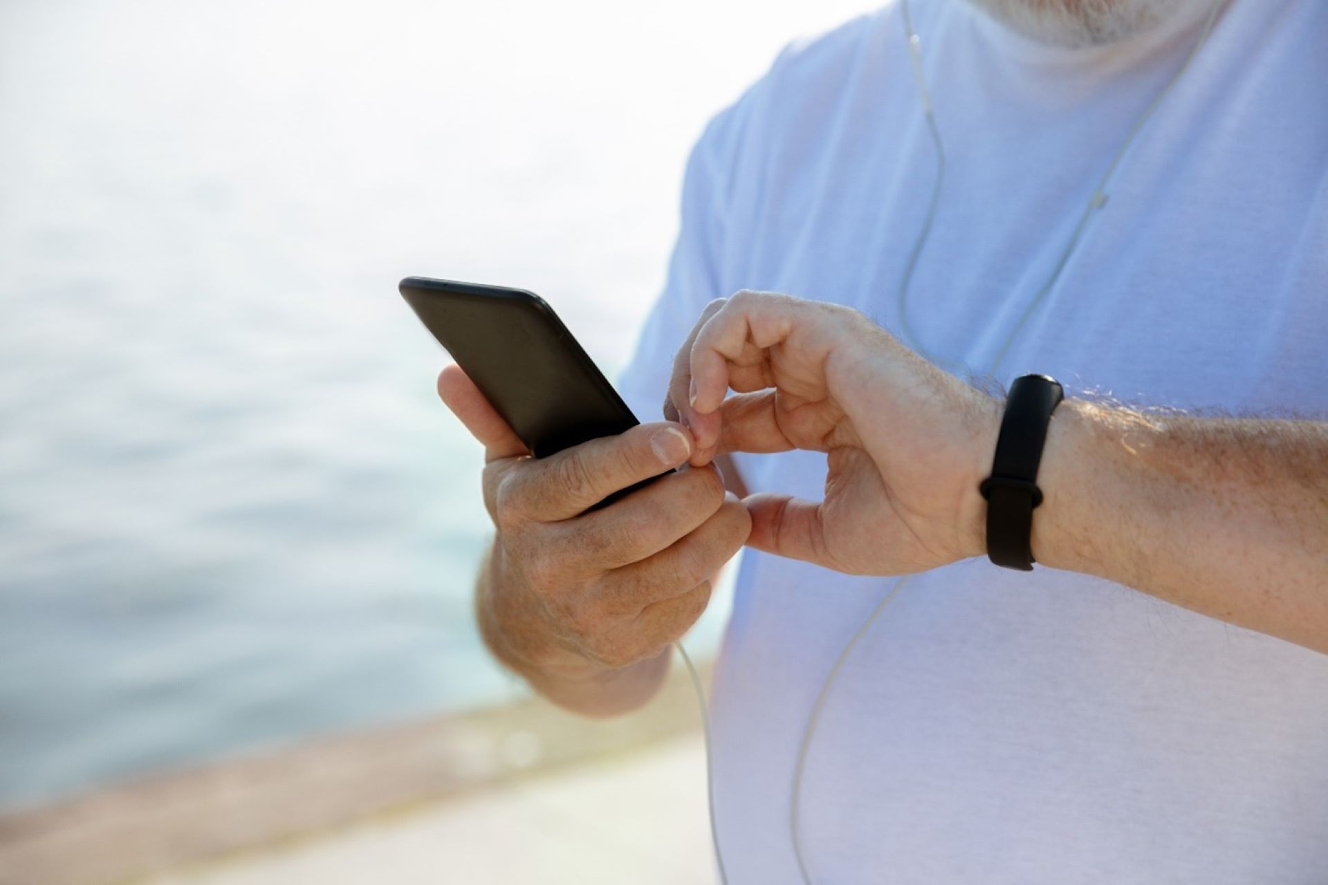 Mann som sjekker pulsklokke og smarttelefon, vann i bakgrunnen. 