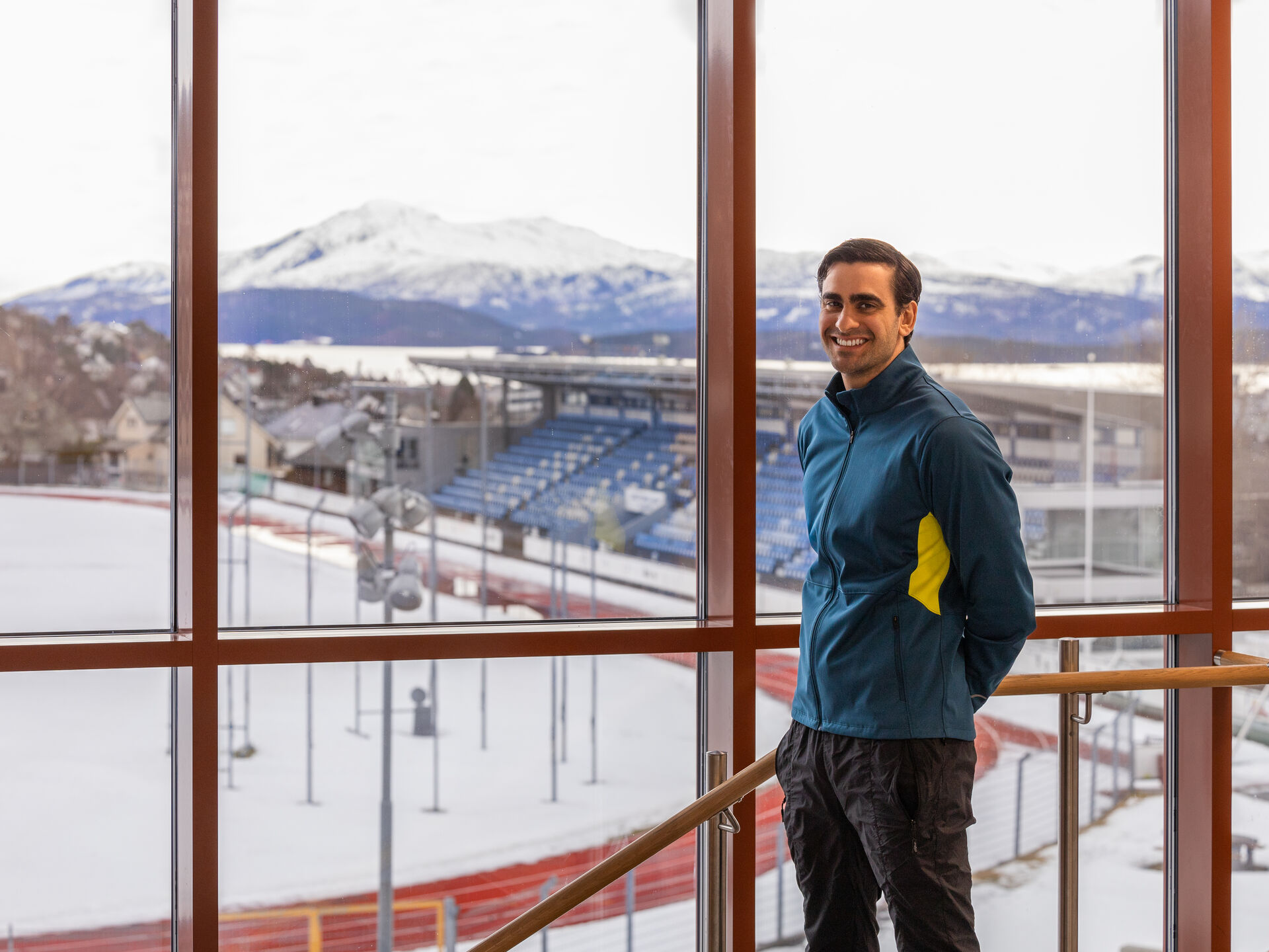 A man standing by a window, overlooking a sport arena