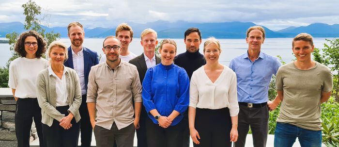 Gruppebilde av forskningsgruppa i fysiologi ved Høgskolen i Molde. De står utendørs på campus Molde med fjellpanorama og fjord i bakgrunnen. 