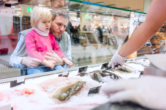 Far og barn ser på utvalg av fisk i en ferskvaredisk. 