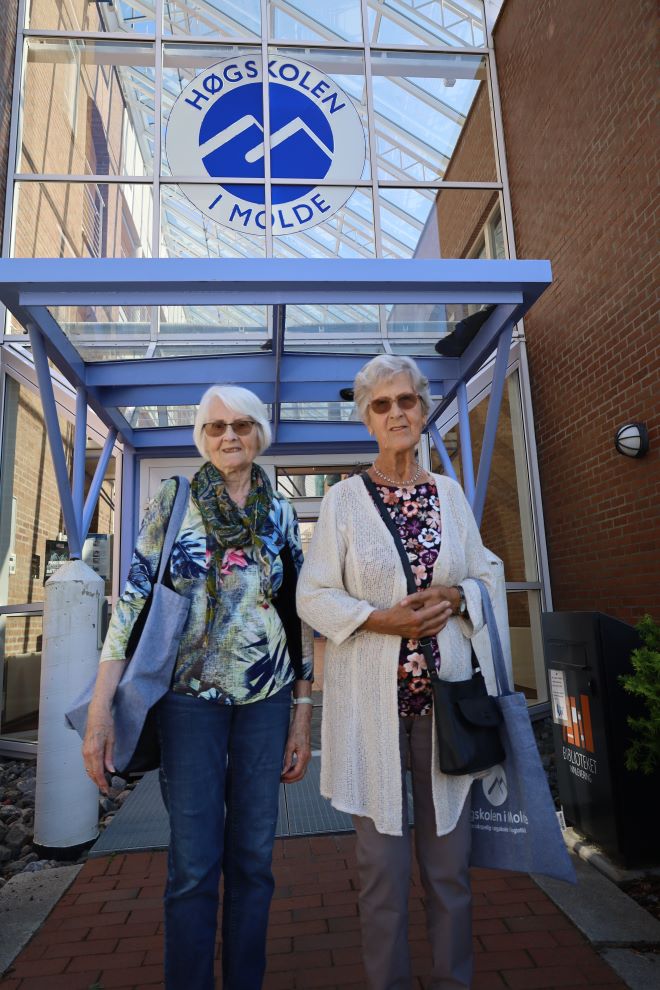 To eldre kvinner foran inngangspartiet til Høgskolen i Molde. De to er tidligere sykepleierstudenter.