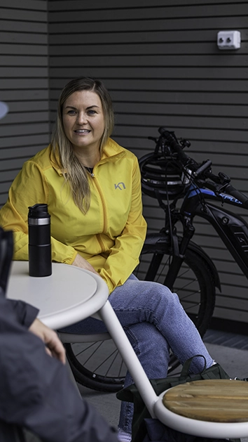 Dame sitter og drikker kaffe ute foran en sykkel