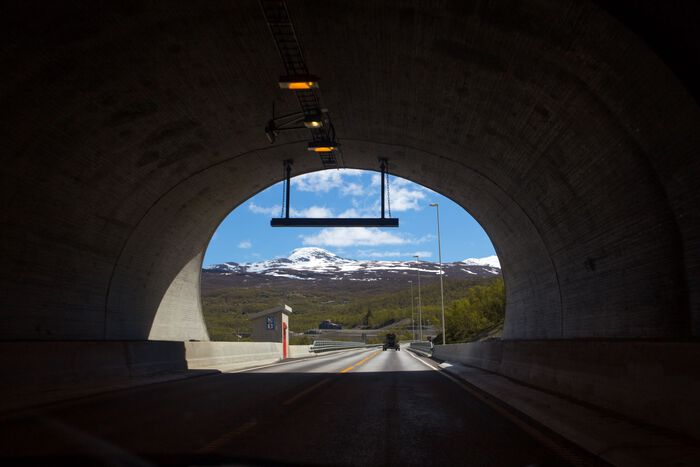 Foto av utgangen til en mørk tunell, sett fra inn i tunell ut mot norsk natur. 