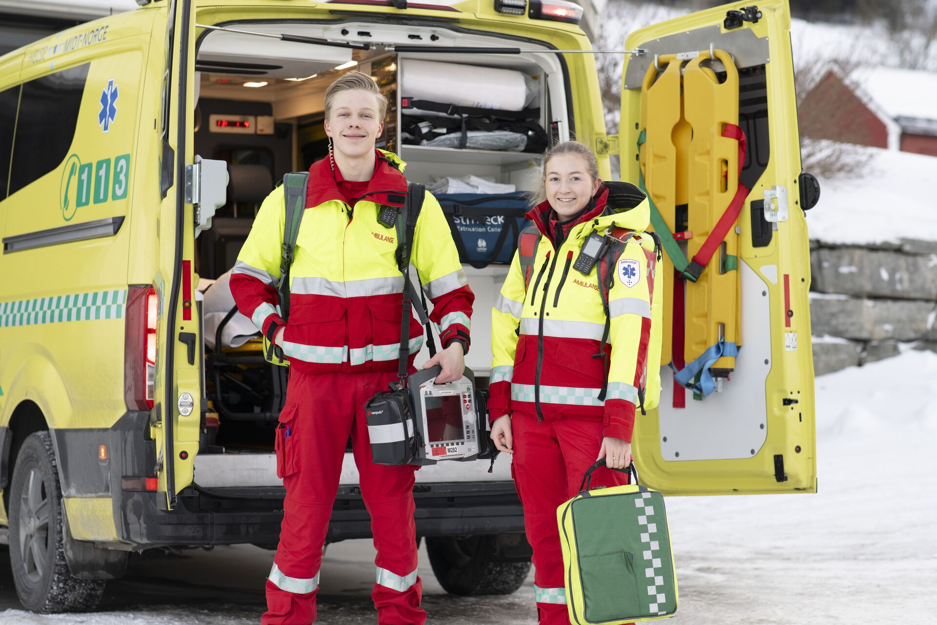 Paramedisiner foran en sykebil. Hun er en ung kvinne, med to uniformer på, for å vise at hun både er klar for uttrykning og for arbeid inne på sykehus. 